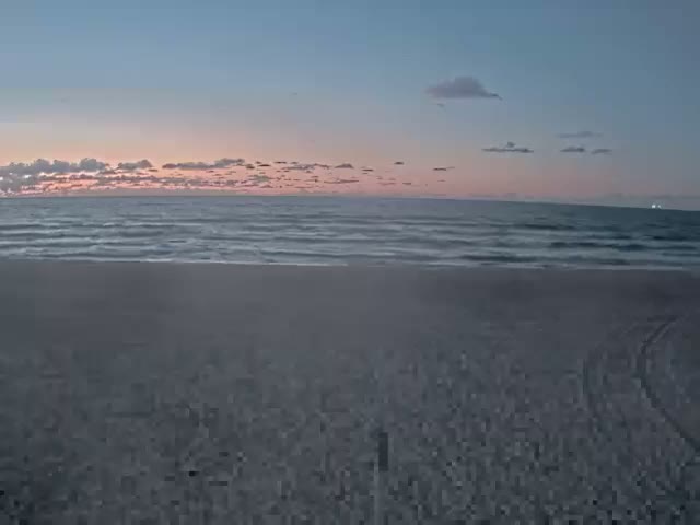 A serene coastal scene features a sandy beach leading to a gently wavy ocean under a twilight sky with scattered clouds, displaying soft blue and pink hues.