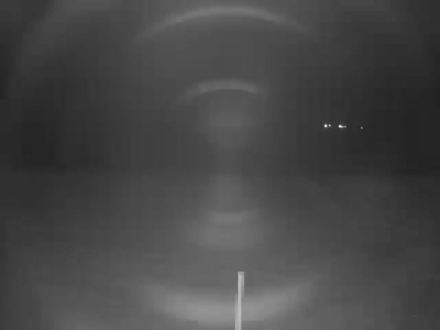 A sandy beach stretches towards a blue ocean with gentle waves under a partially cloudy sky, indicating fair weather.