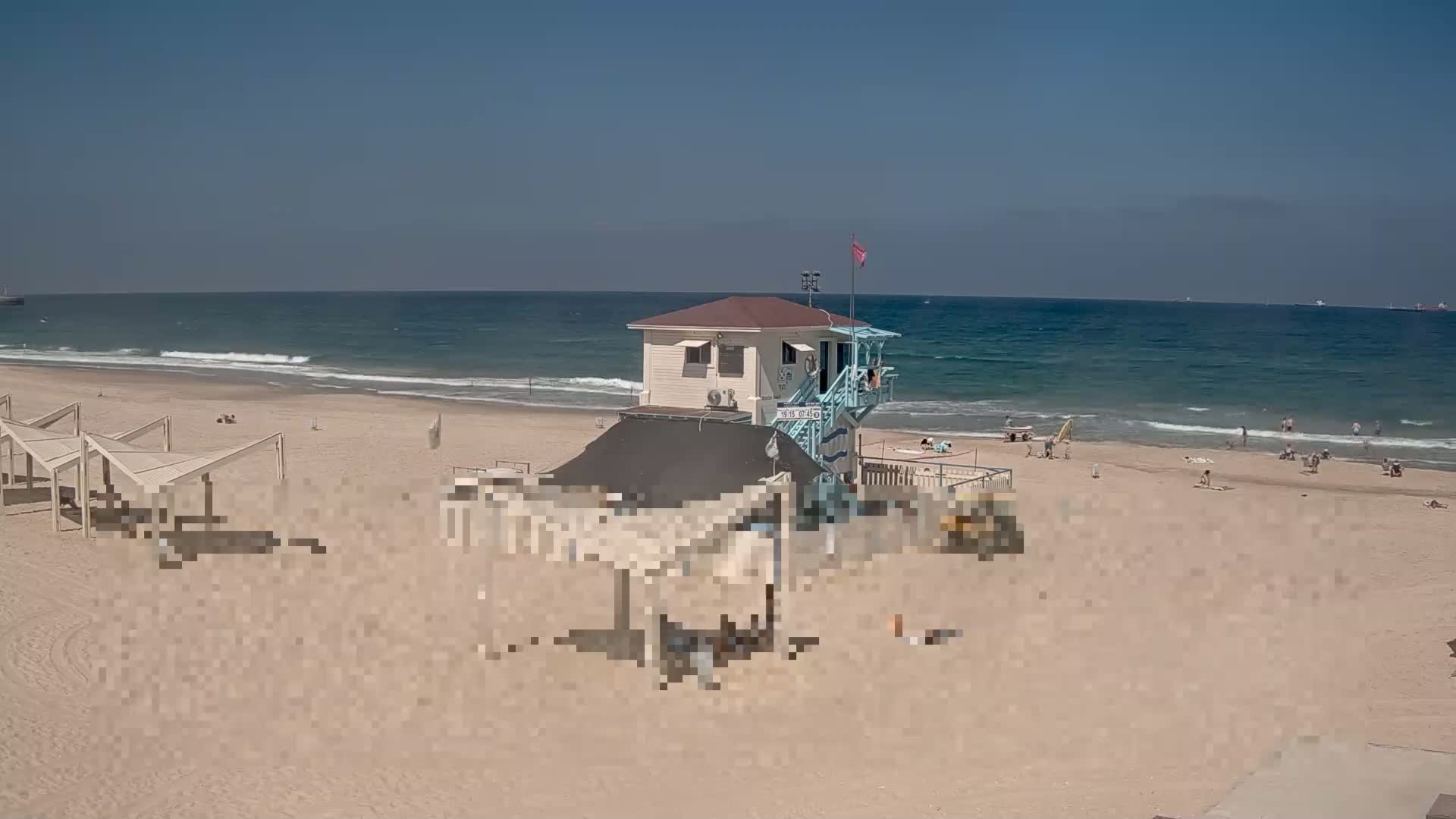 A lifeguard station sits on a sandy beach with a calm ocean under a clear blue sky.