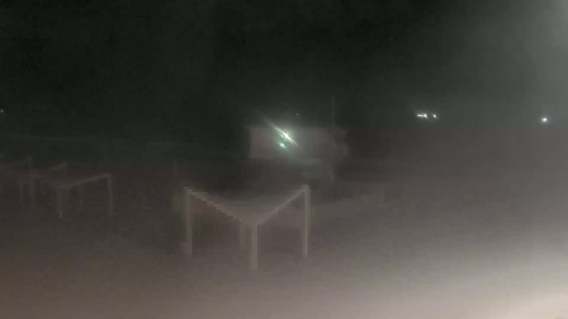 Several empty tables are visible in a hazy, dark outdoor space at night.
