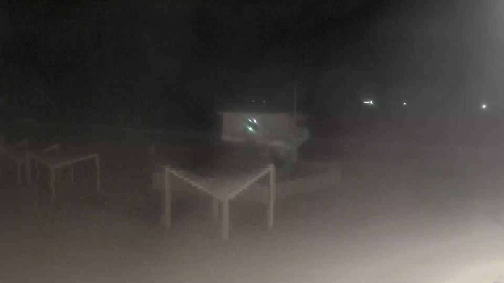 Several empty tables are visible in a hazy, dark outdoor space at night.