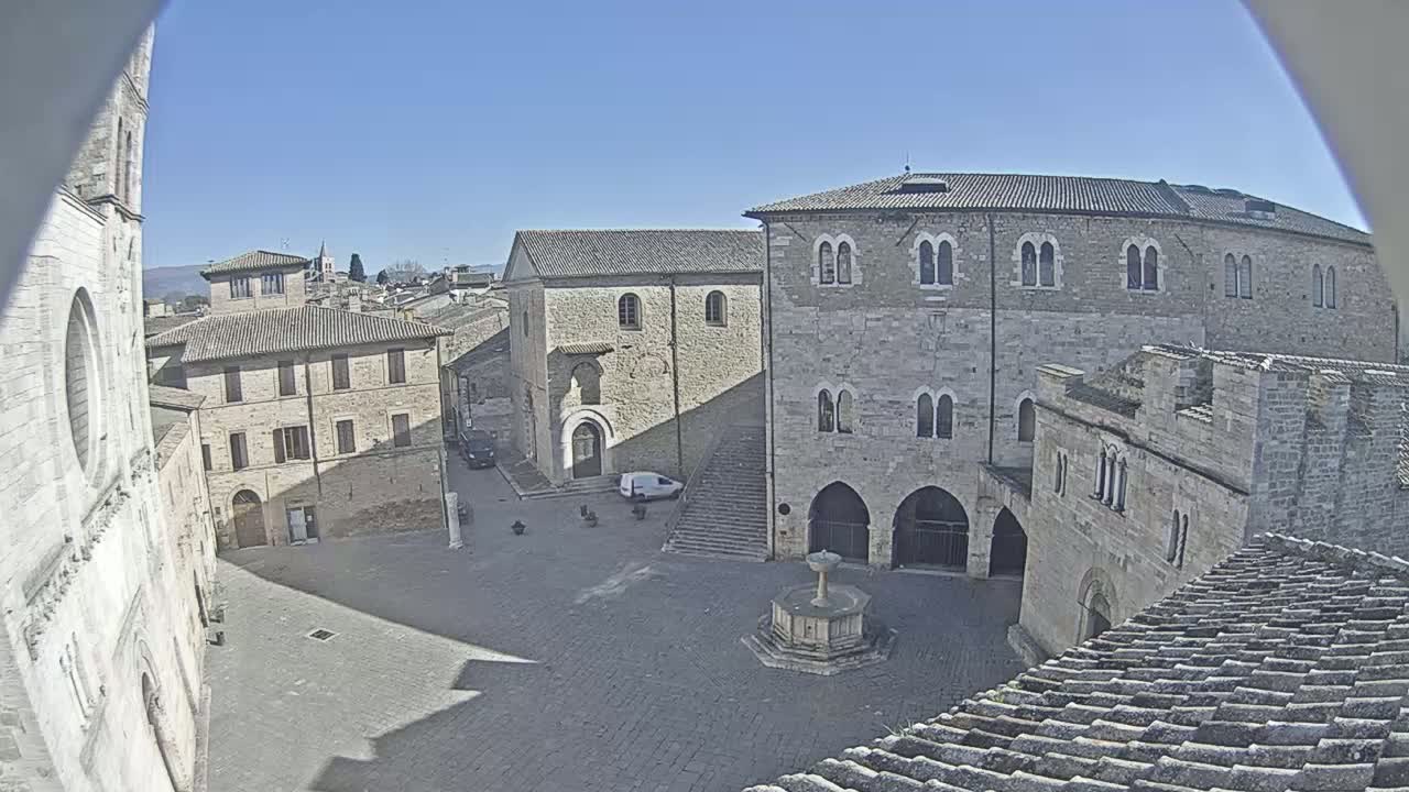 An elevated view shows a town square surrounded by medieval stone buildings under a clear blue sky.