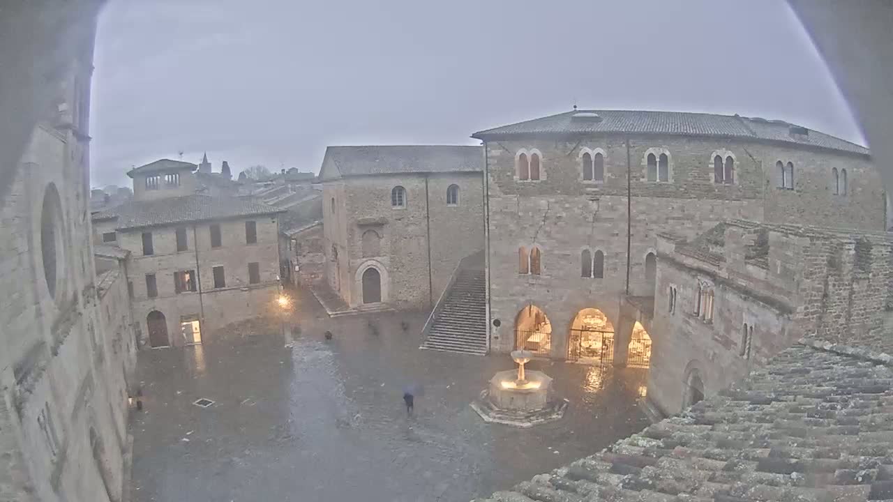 A rain-soaked town square, surrounded by old stone buildings, features a central fountain.