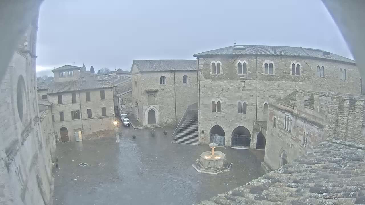 A rain-soaked town square, surrounded by old stone buildings, features a central fountain.