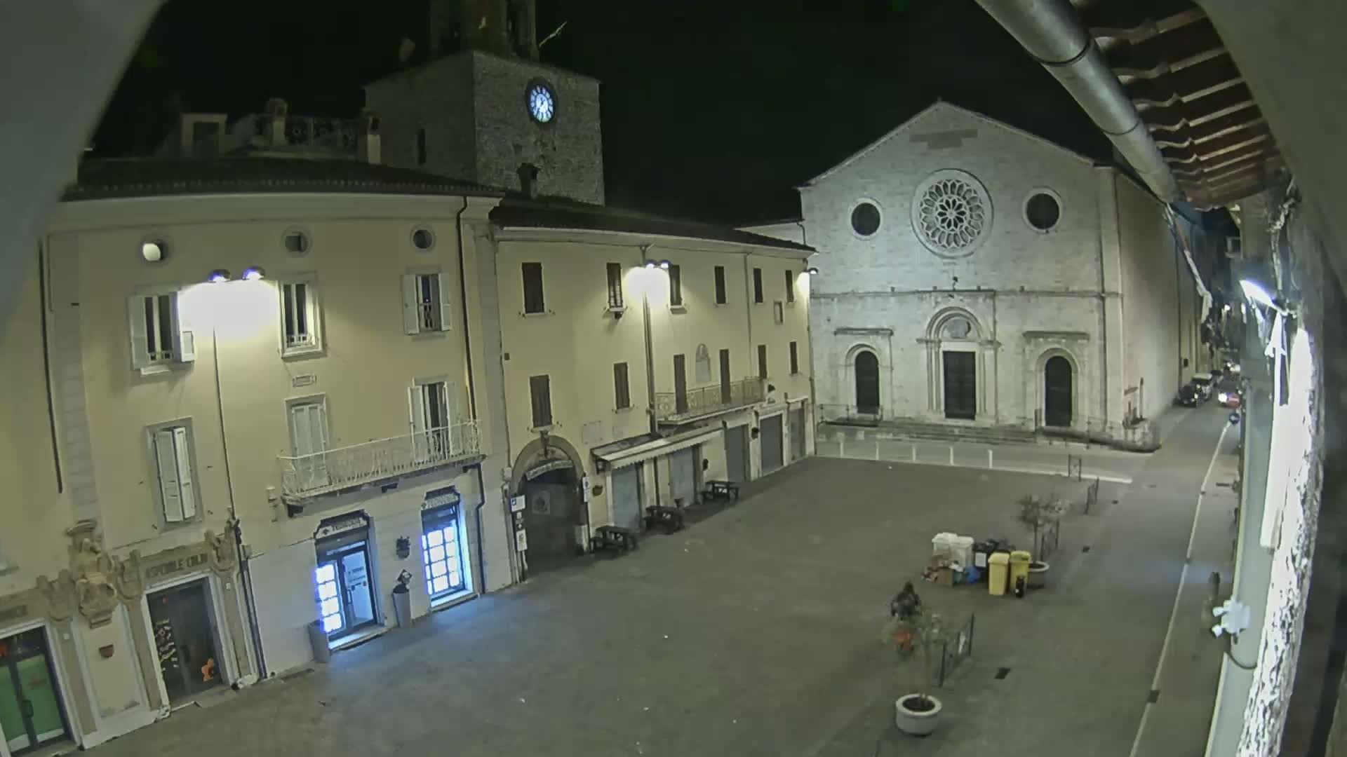A nighttime, high-angle view of a town square with several buildings, including a church with a rose window, under dark conditions.
