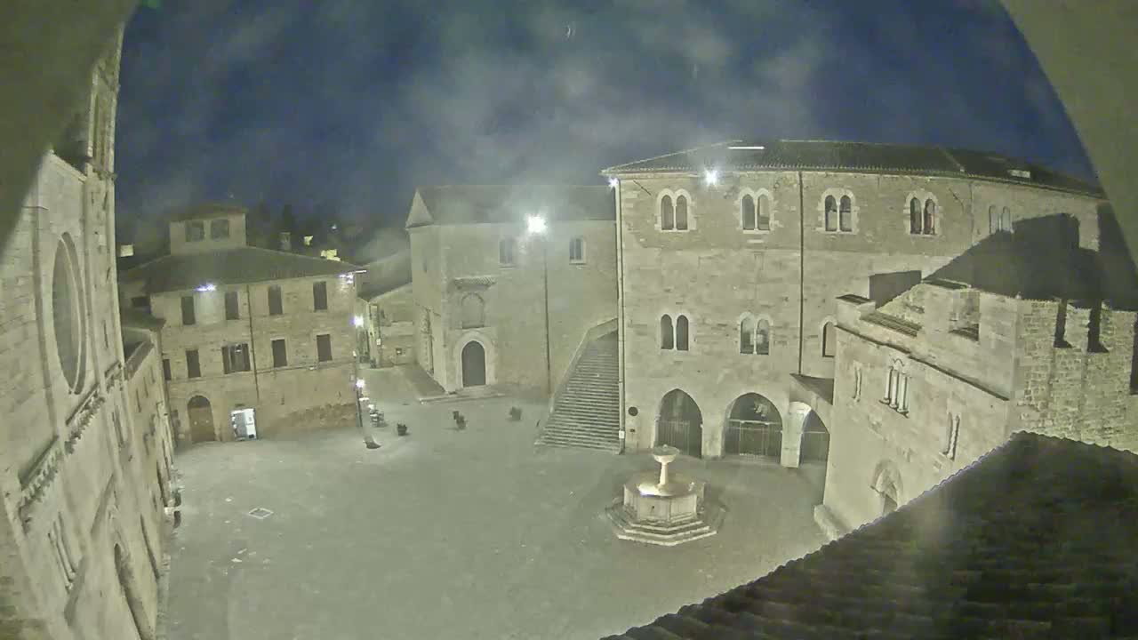 A nighttime view of a stone plaza with buildings surrounding it, under a slightly hazy sky.