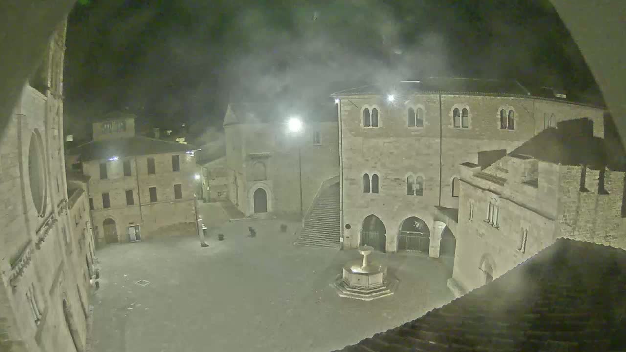 A nighttime view of a town square with several stone buildings surrounding it, under hazy or foggy conditions.