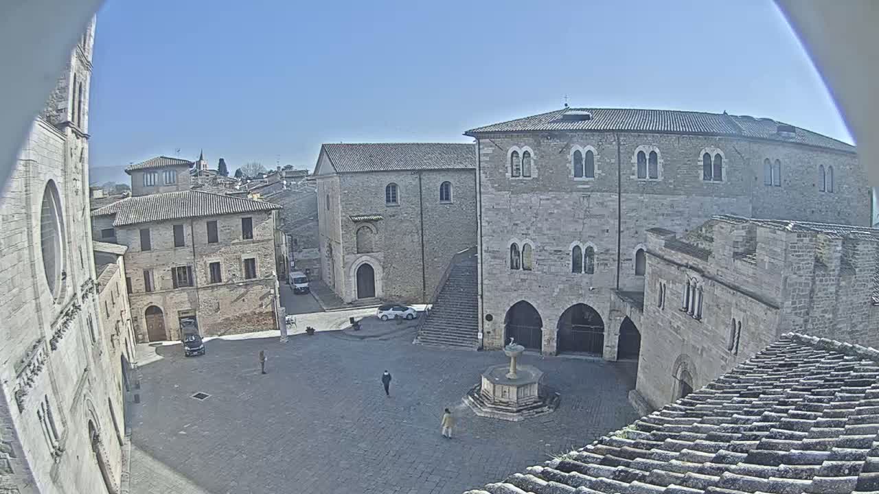 A sunny view of a town square in Italy, surrounded by aged stone buildings, features a fountain in the center.