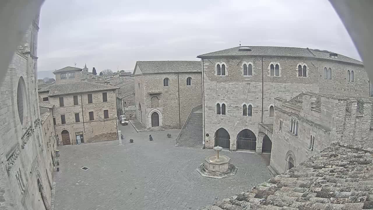 A stone plaza with a fountain is surrounded by aged, multi-story buildings on an overcast day.