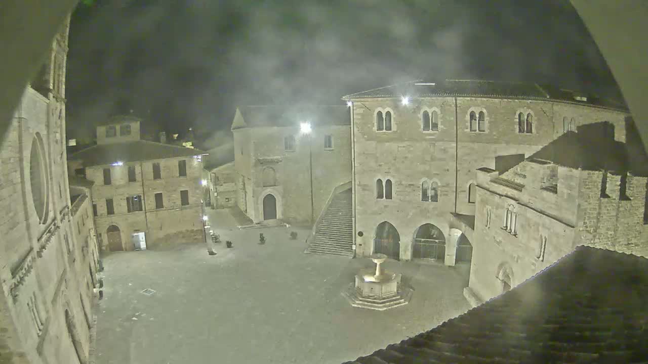 A nighttime view of a stone plaza, surrounded by medieval-style buildings under a hazy or foggy sky.