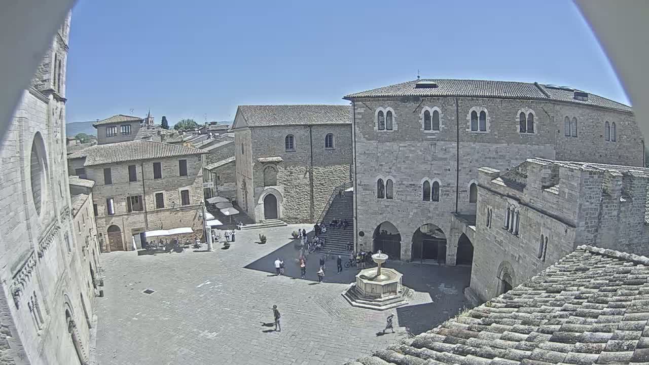 A sun-drenched town square, surrounded by historic stone buildings, features a central fountain and a scattering of people.
