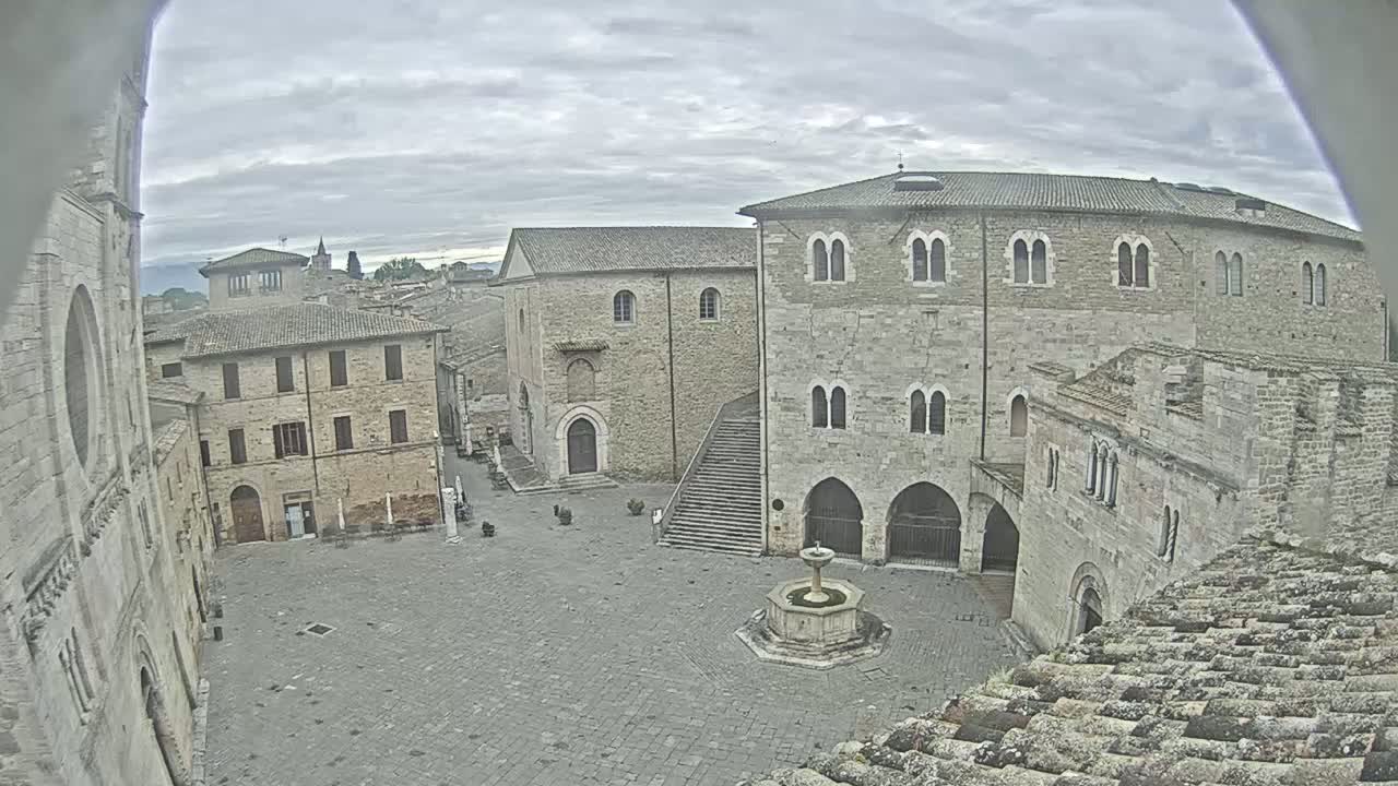 A mostly empty cobblestone square is surrounded by aged stone buildings under an overcast sky.