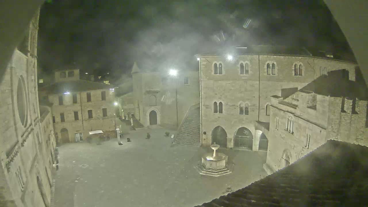 A nighttime view of a town square with several stone buildings surrounding a fountain.