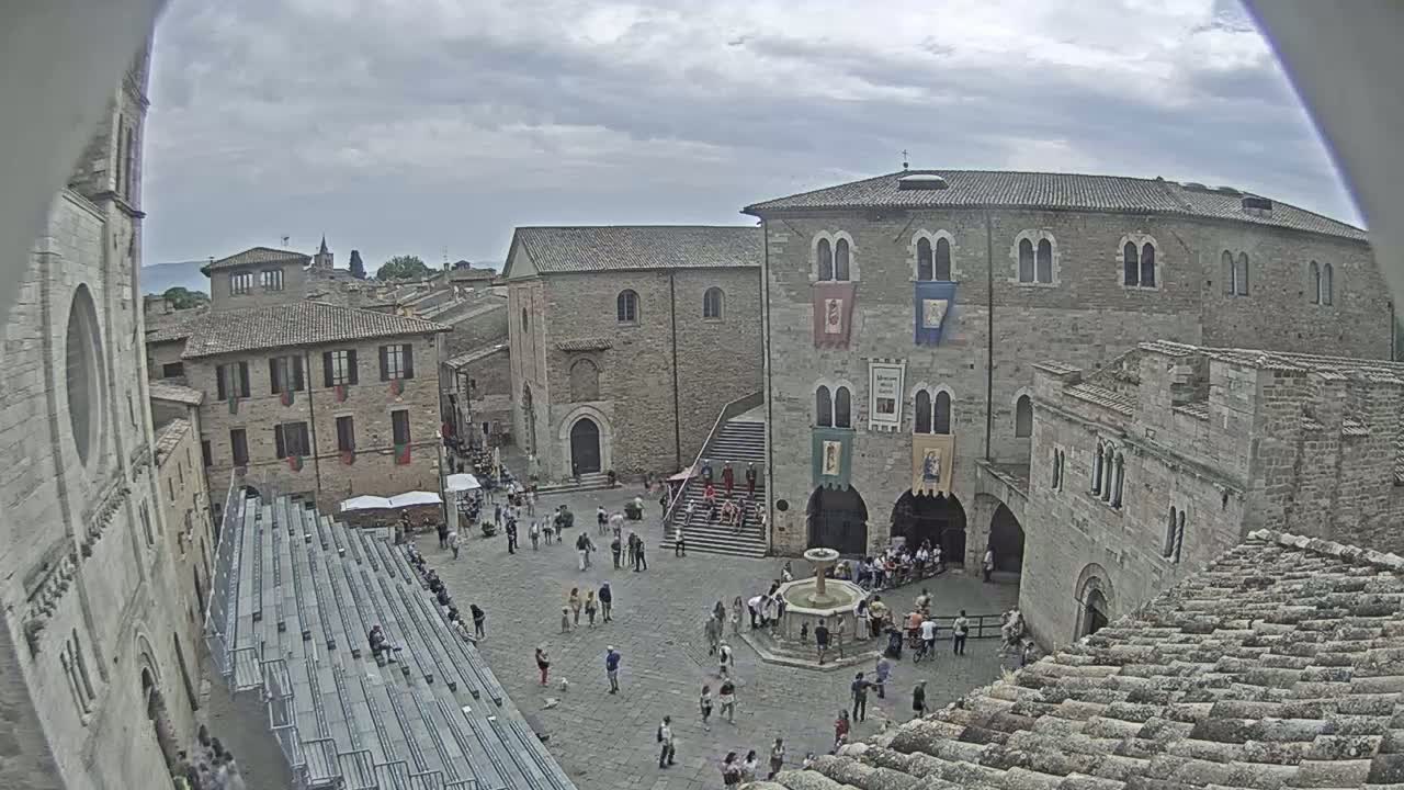 A town square, surrounded by medieval-style buildings, is populated with people on an overcast day.
