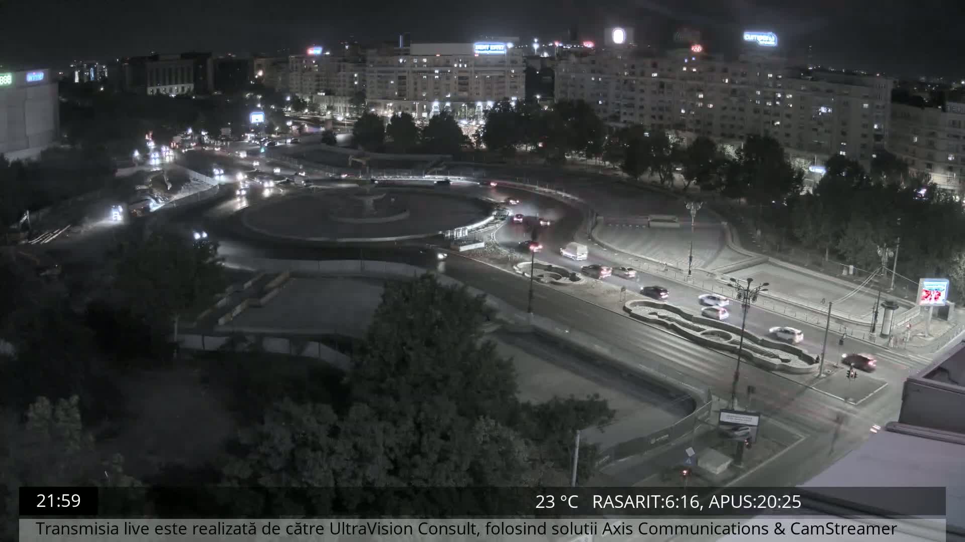 A nighttime aerial view shows a city roundabout with moderate traffic under clear skies.