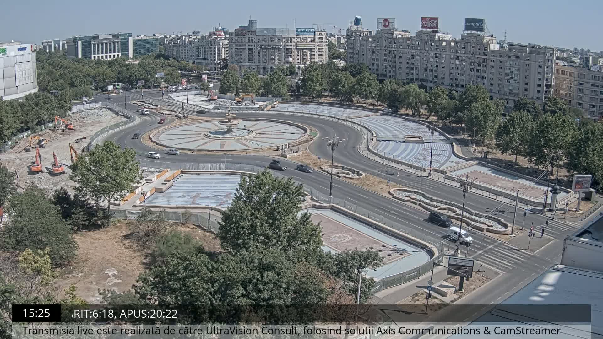 A nighttime aerial view shows a city roundabout with moderate traffic under clear skies.