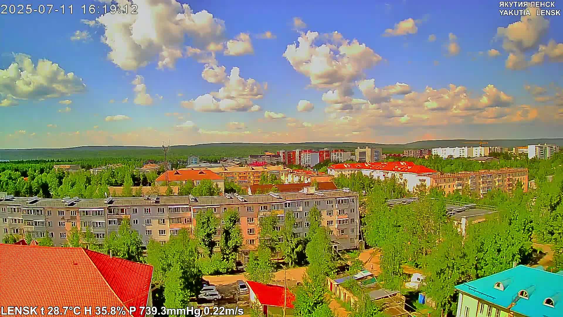 A partly cloudy summer day overlooks a residential area with multi-story buildings and lush green trees.
