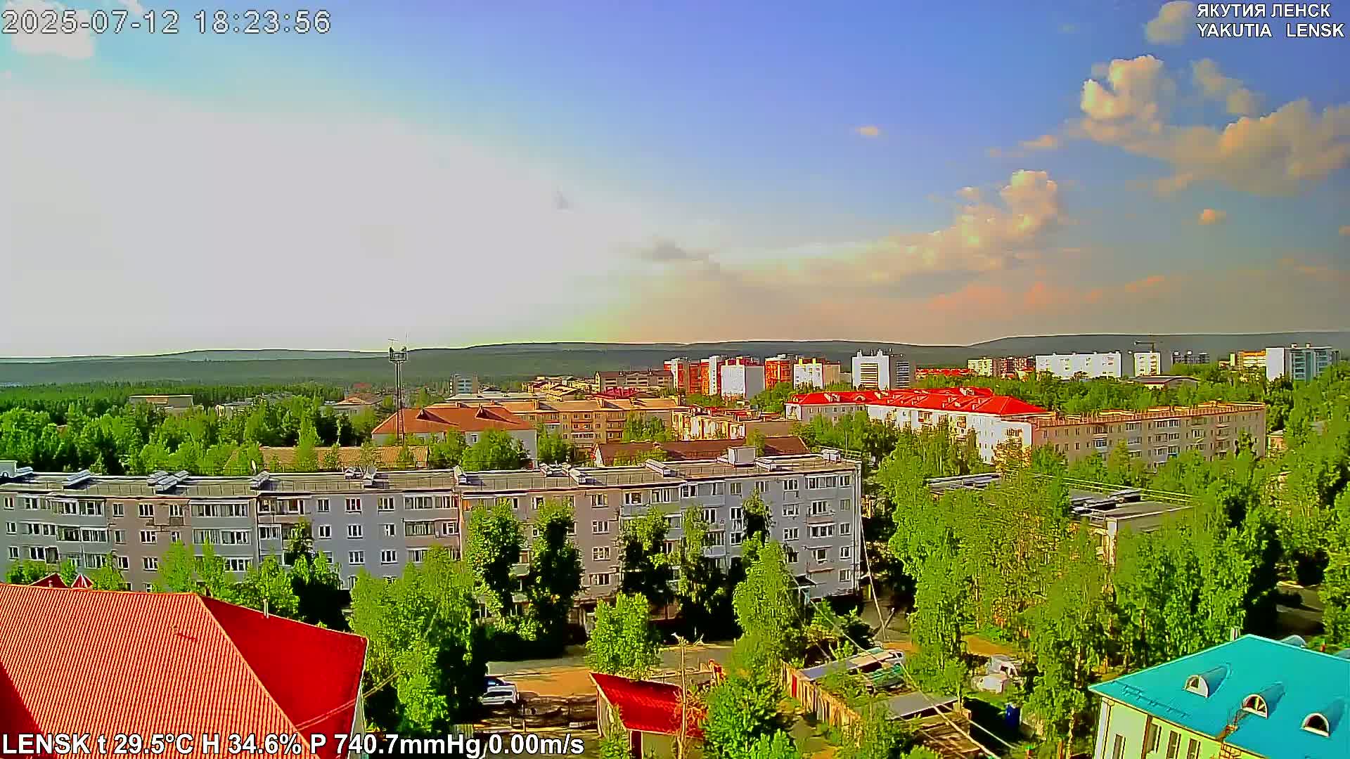 A partly cloudy summer day overlooks a residential area with multi-story buildings and lush green trees.