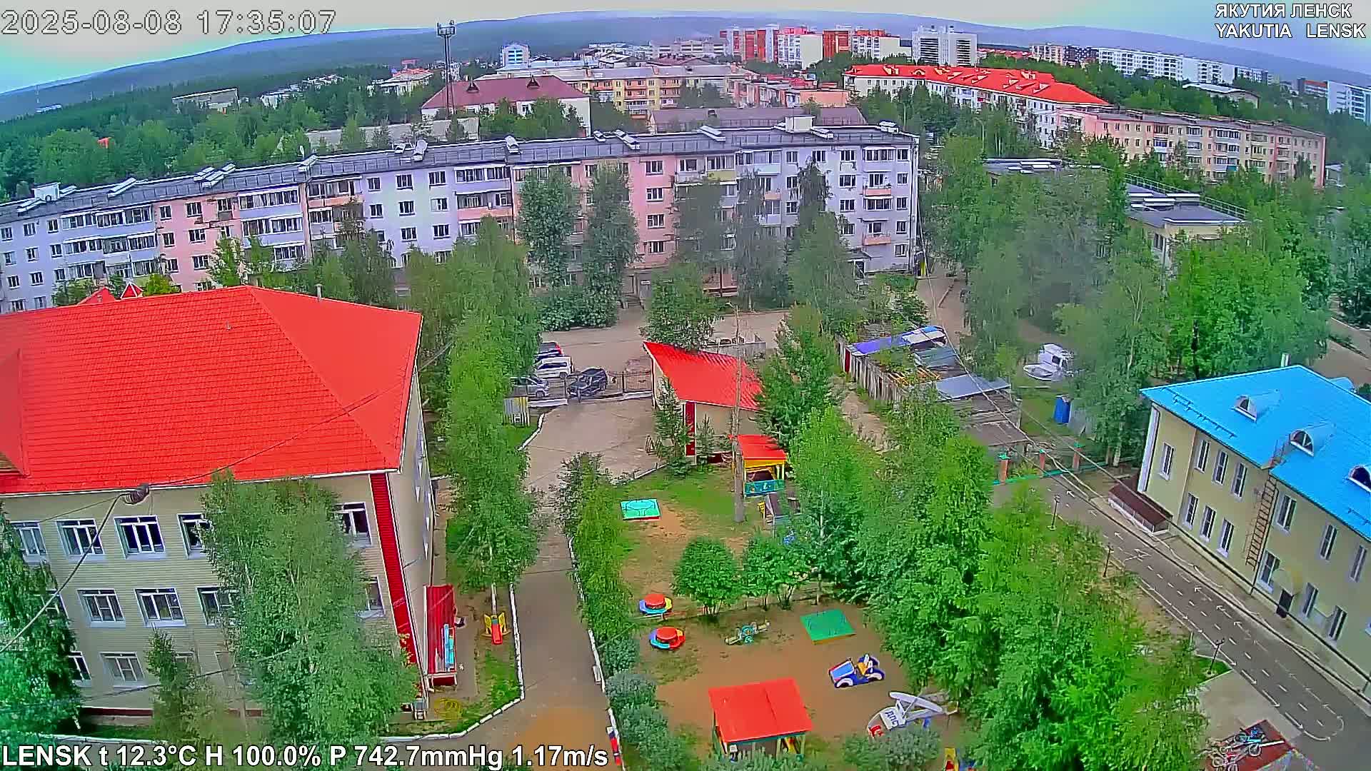 An aerial view shows a residential area with apartment buildings, a playground with colorful equipment, and overcast weather.