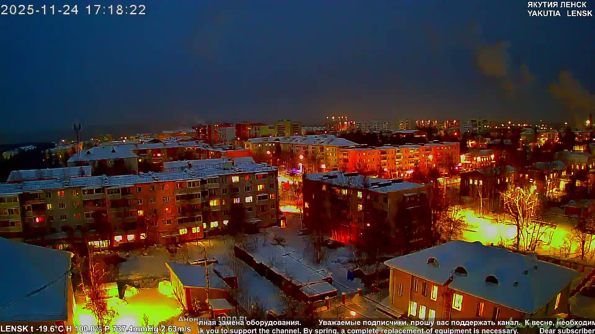 A snow-covered city unfolds at night, with buildings and streets aglow from numerous artificial lights under a clear, dark blue sky, indicating very cold winter conditions.