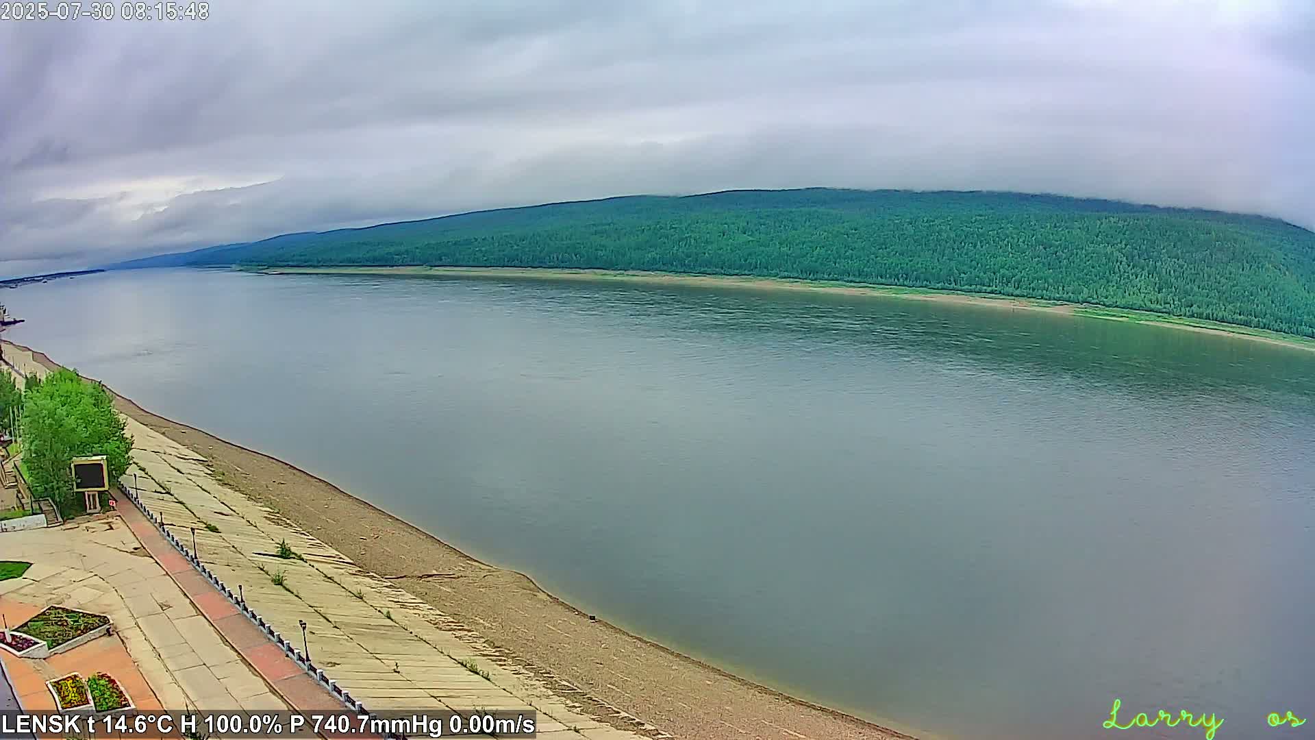 A calm river reflects a verdant hillside under a partly cloudy sky.