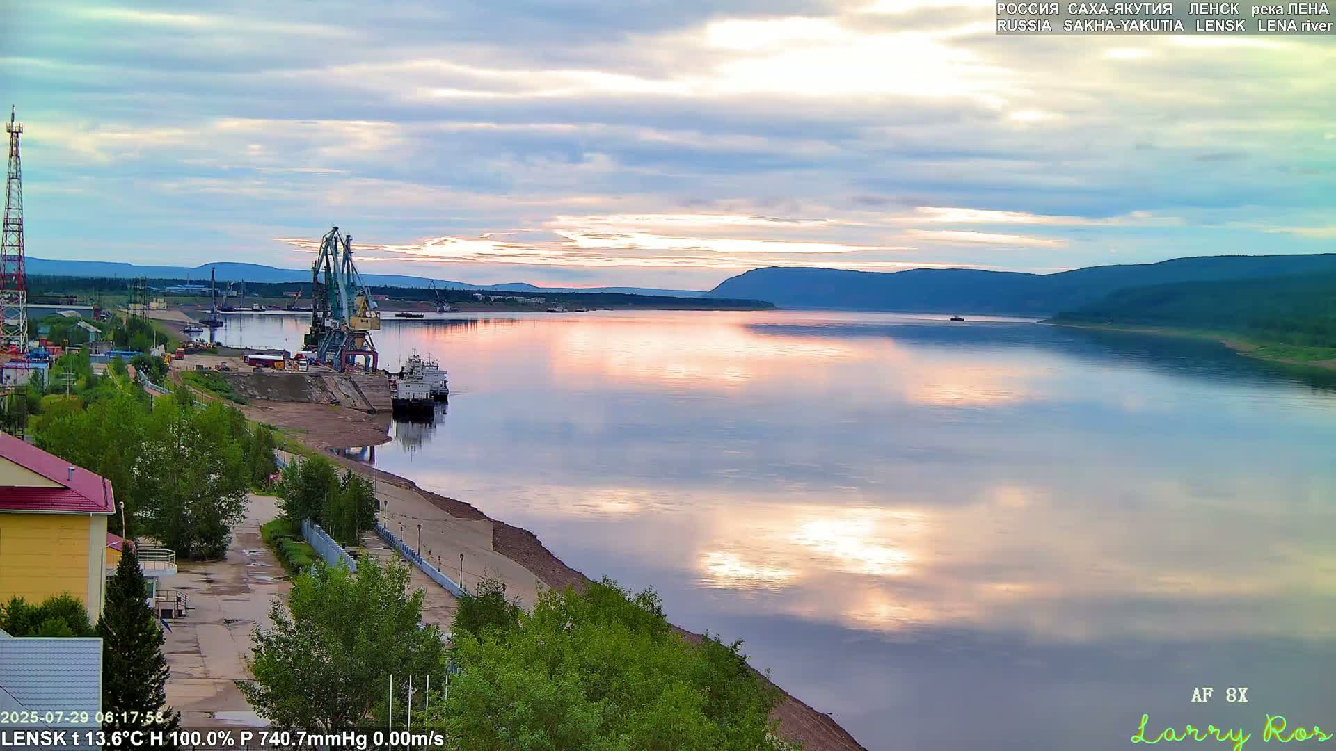 A calm river reflects a pastel sunrise sky, with a port and industrial cranes visible along the shore.