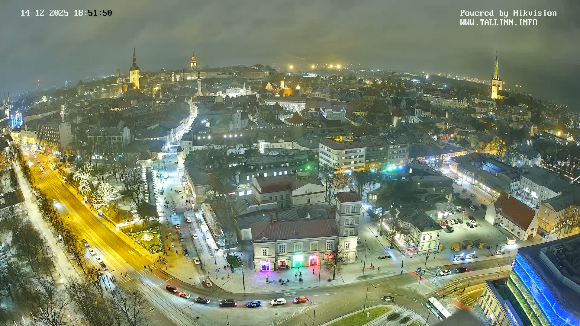 A foggy, overcast day blankets a sprawling European city, revealing a vibrant mix of historical and modern buildings with numerous red roofs, wet streets bustling with traffic and pedestrians, and distant steeples fading into the haze.