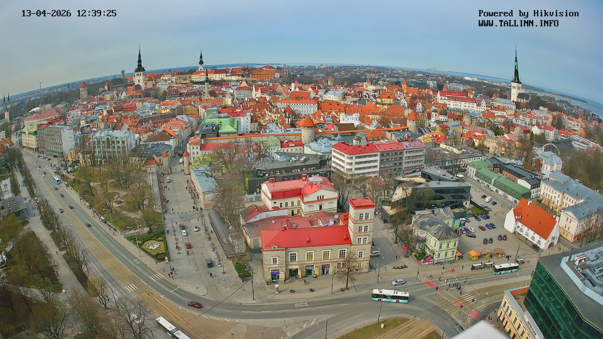 A foggy, overcast day blankets a sprawling European city, revealing a vibrant mix of historical and modern buildings with numerous red roofs, wet streets bustling with traffic and pedestrians, and distant steeples fading into the haze.