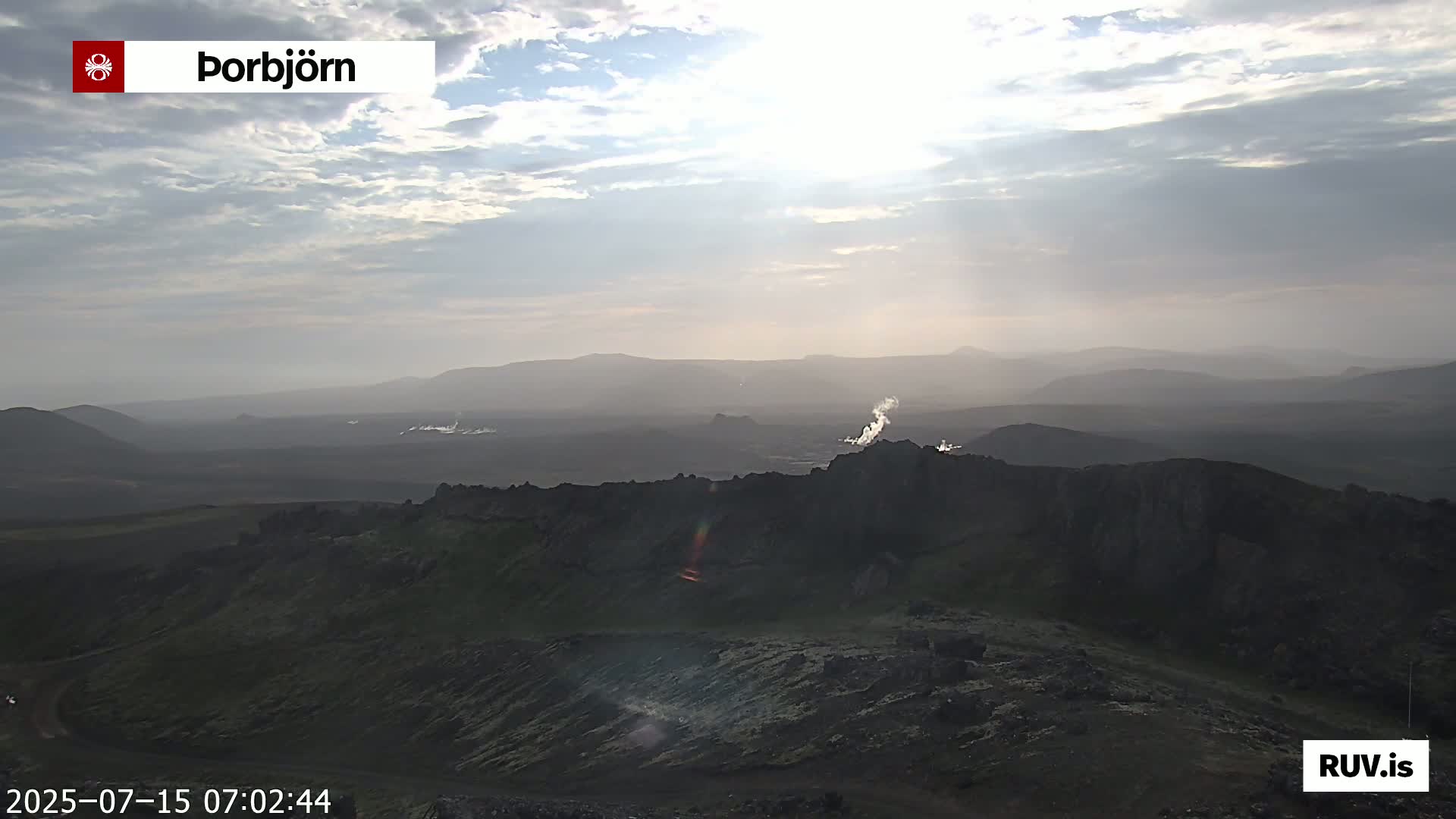 A sunlit, hazy volcanic landscape with steam rising from vents in the distance.
