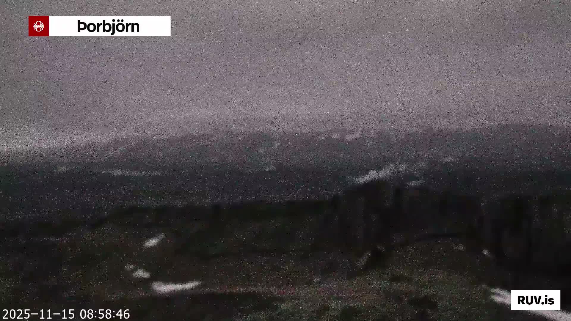 A dark, grainy, and hazy view reveals a mountainous landscape with scattered patches of snow under a heavily overcast and gloomy sky.