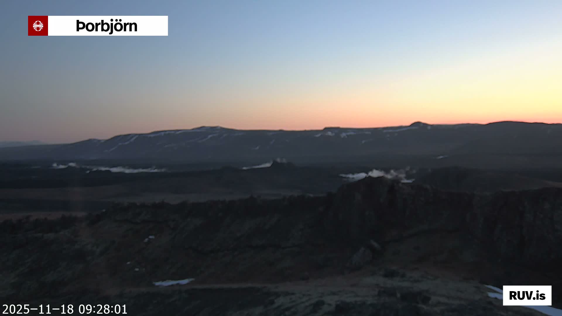 A dark, grainy, and hazy view reveals a mountainous landscape with scattered patches of snow under a heavily overcast and gloomy sky.
