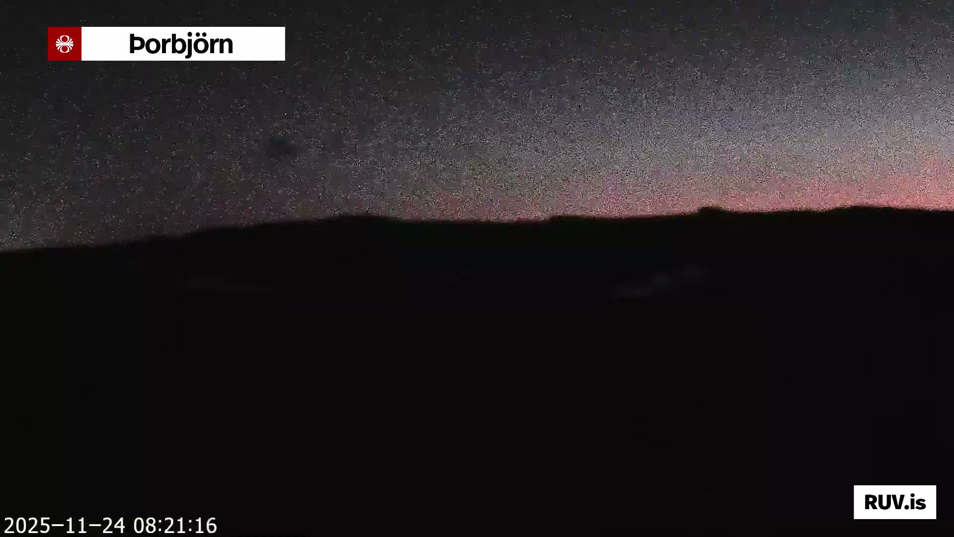 A vast, dark, and silhouetted mountainous landscape is visible under a faintly speckled night sky, with a soft pinkish glow emanating from the horizon, suggesting clear weather conditions.