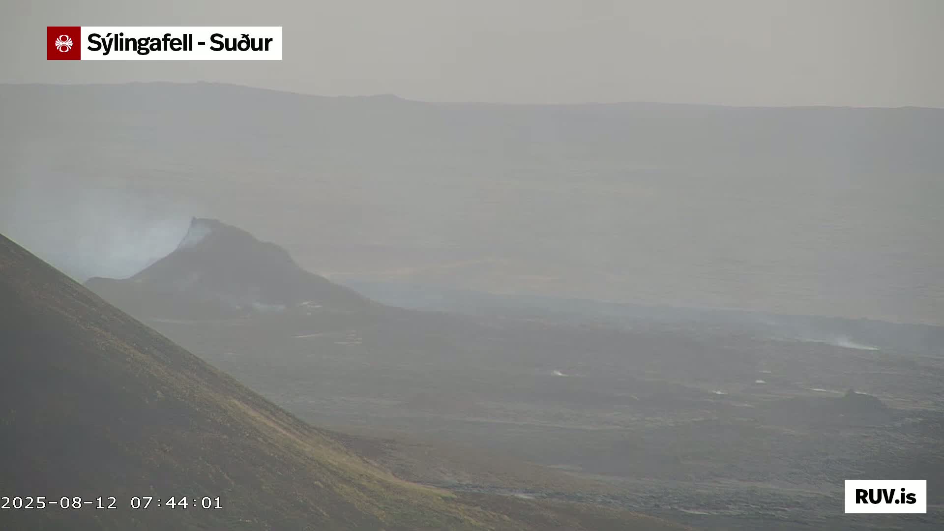 A hazy, volcanic landscape is visible, featuring a dark, steaming hill in the midground and a sloping, dark hill in the foreground.