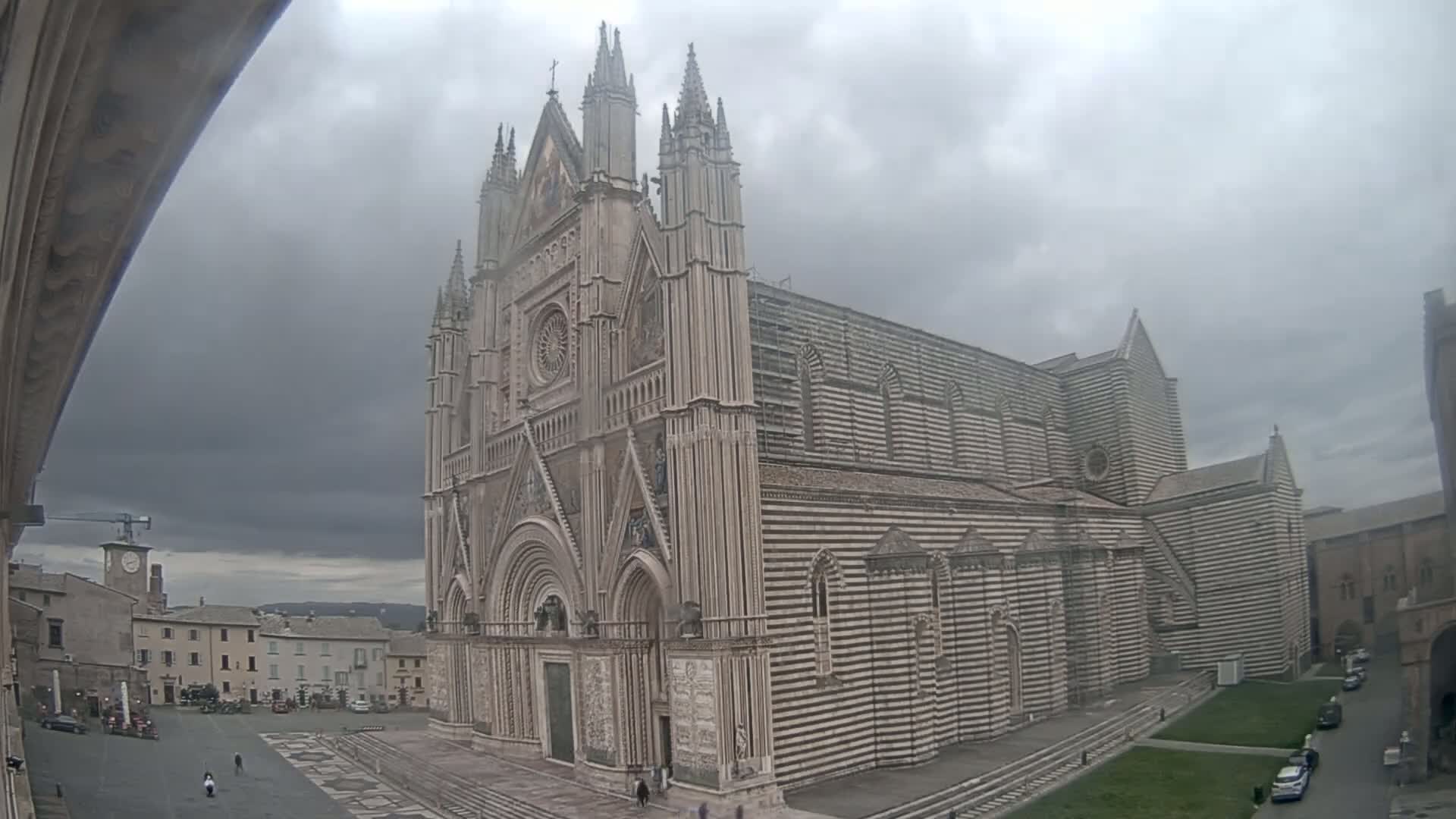 A large, striped cathedral stands in a town square under an overcast sky.