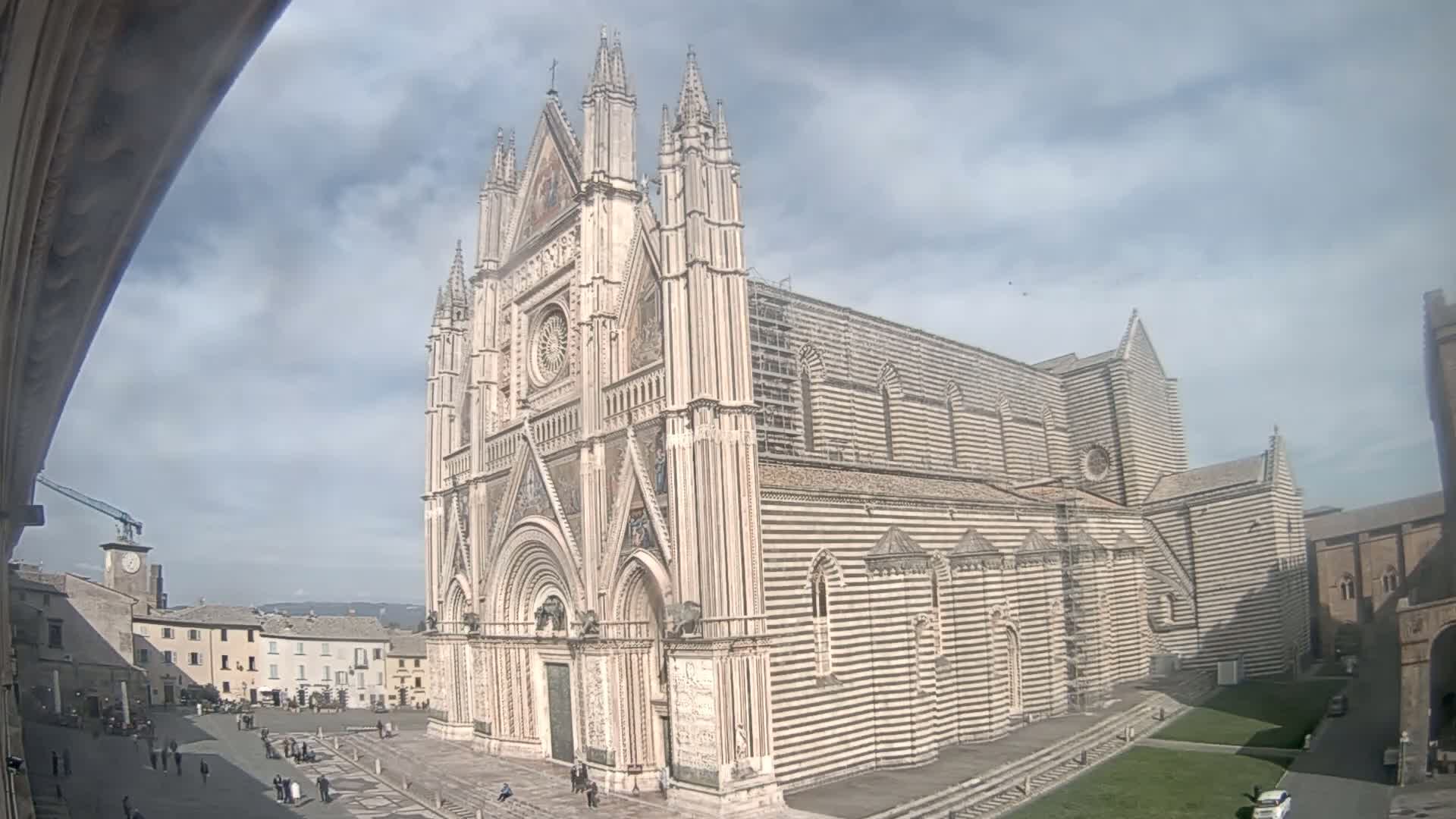 A large, ornate cathedral with striped facade stands in a town square under a partly cloudy sky.