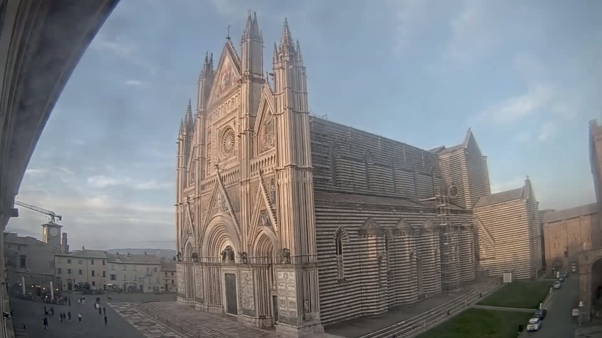 A large striped cathedral stands in a town square under a mostly clear sky.