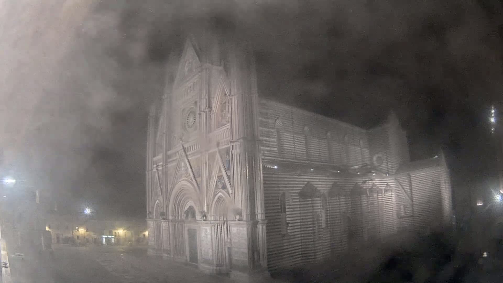 A large, striped stone cathedral is partially obscured by fog at night.