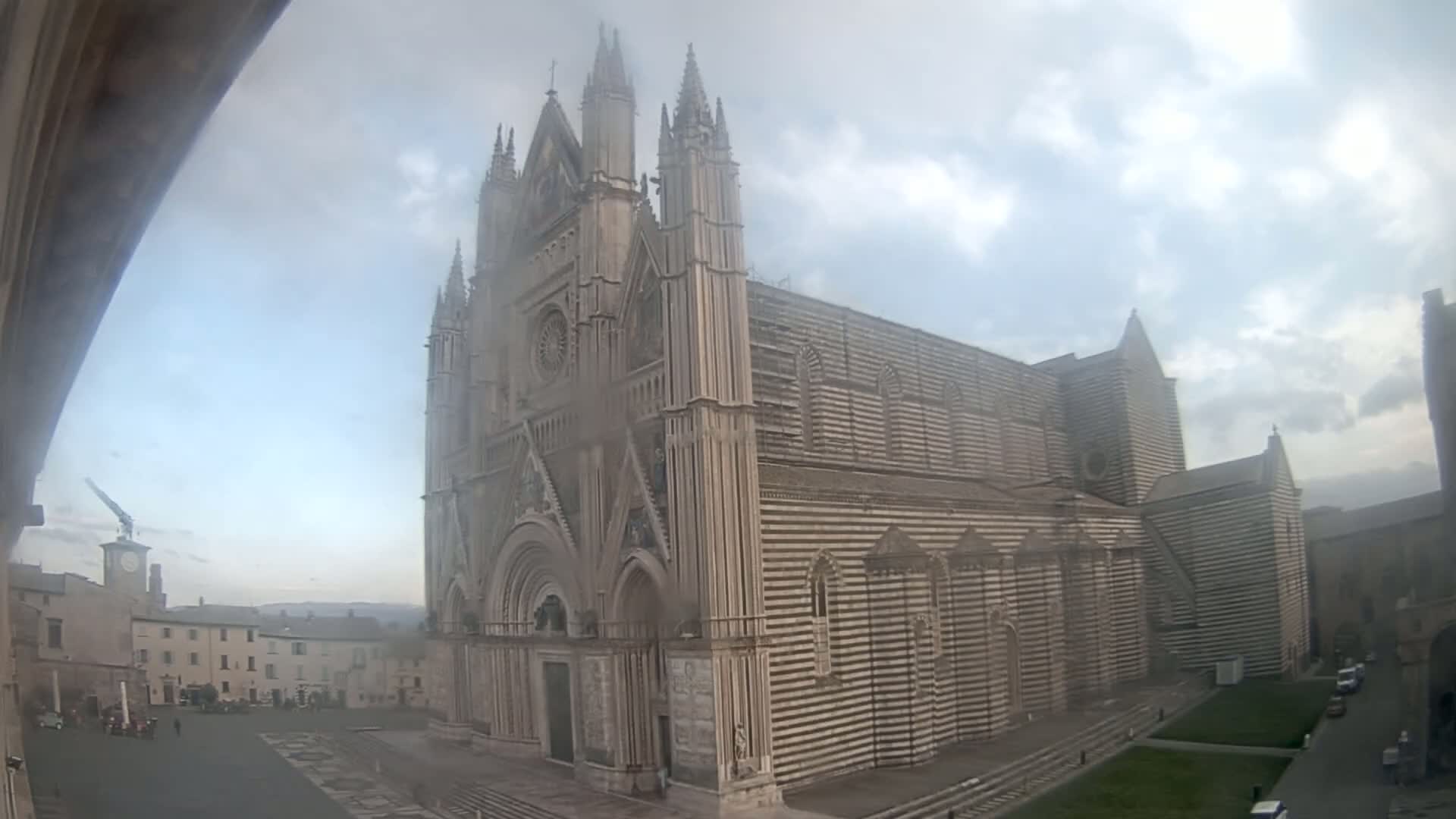 A large, striped stone cathedral stands in a town square under an overcast sky.