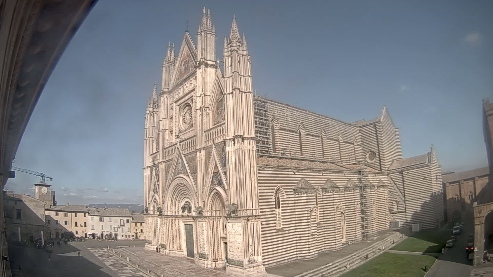 A large, striped cathedral stands in a town square on a sunny day.