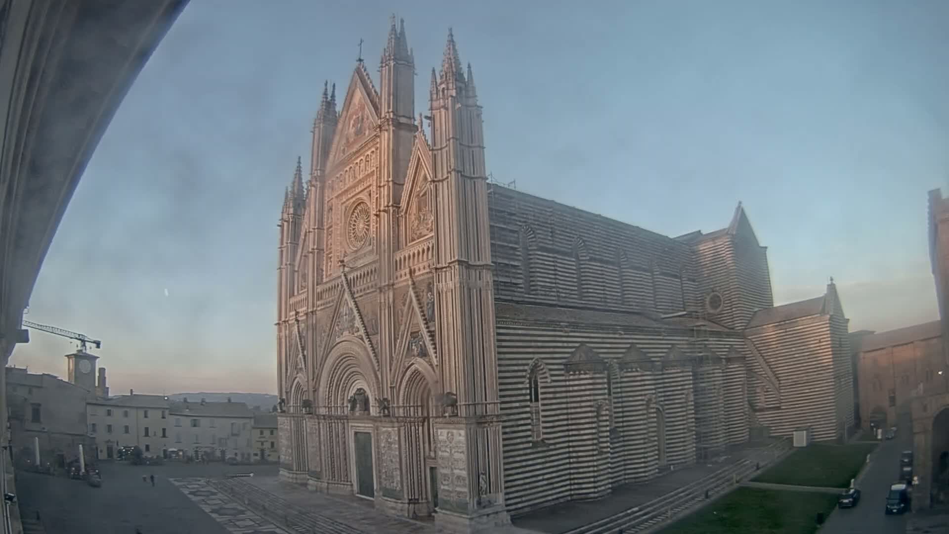 A large, striped cathedral stands in a town square under a clear, pale sky.