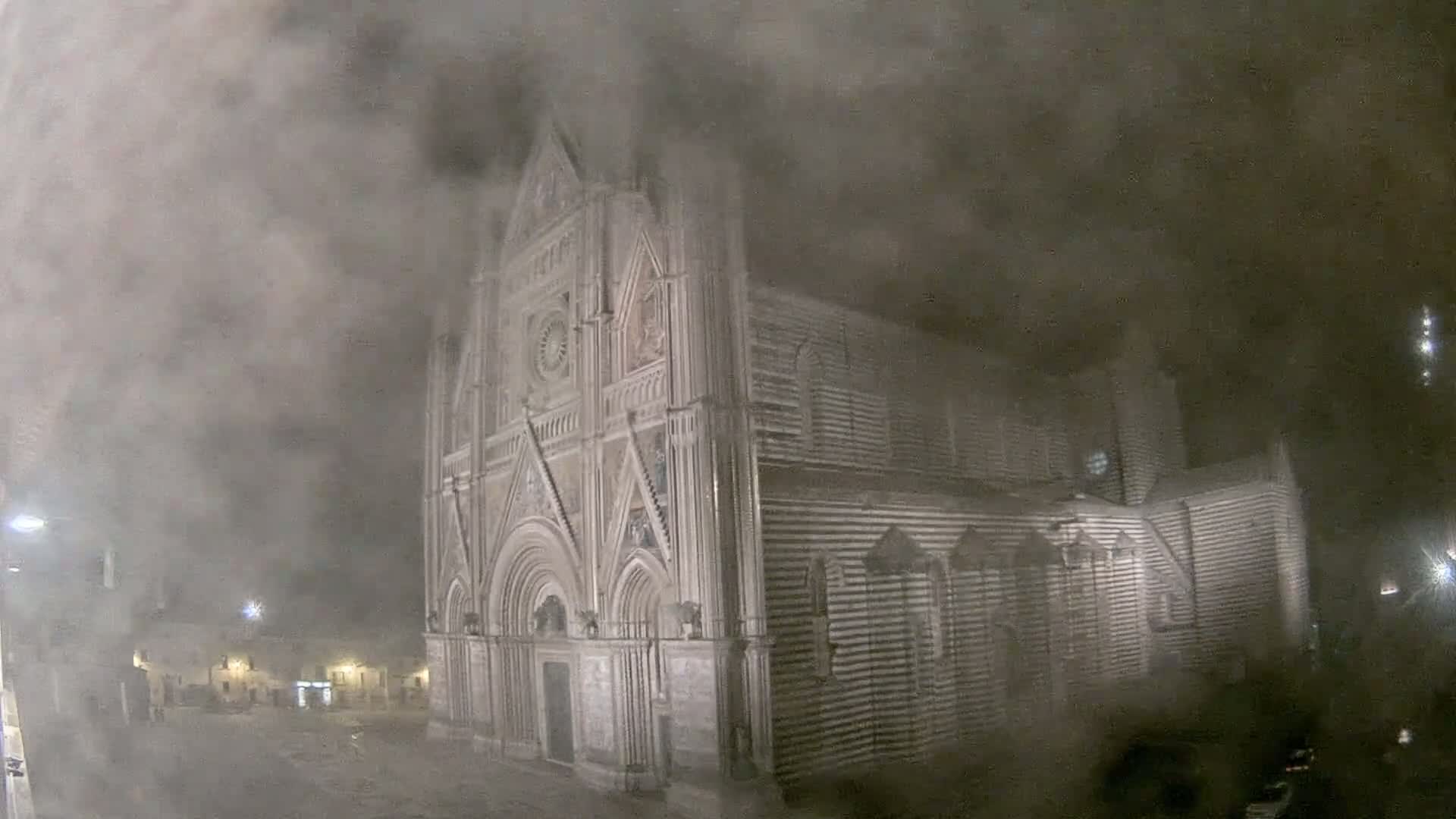 A large stone cathedral is partially obscured by heavy fog or mist at night.