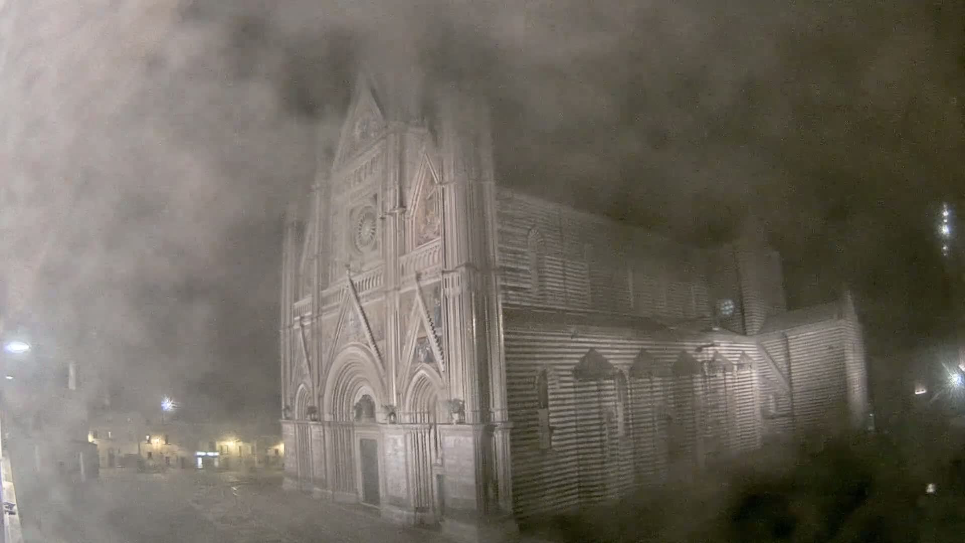 A large, ornate stone cathedral is shrouded in a thick fog at night.