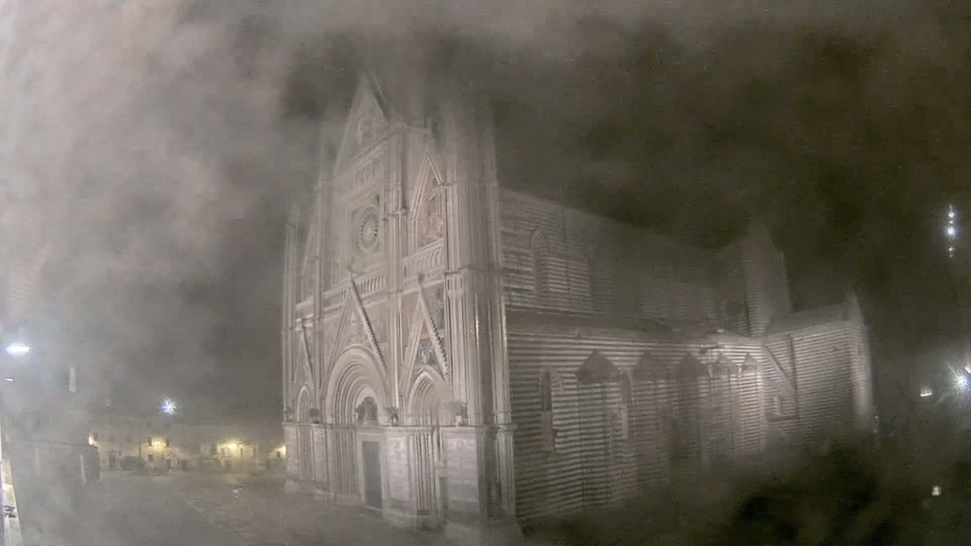 A large stone cathedral is shrouded in thick fog at night.