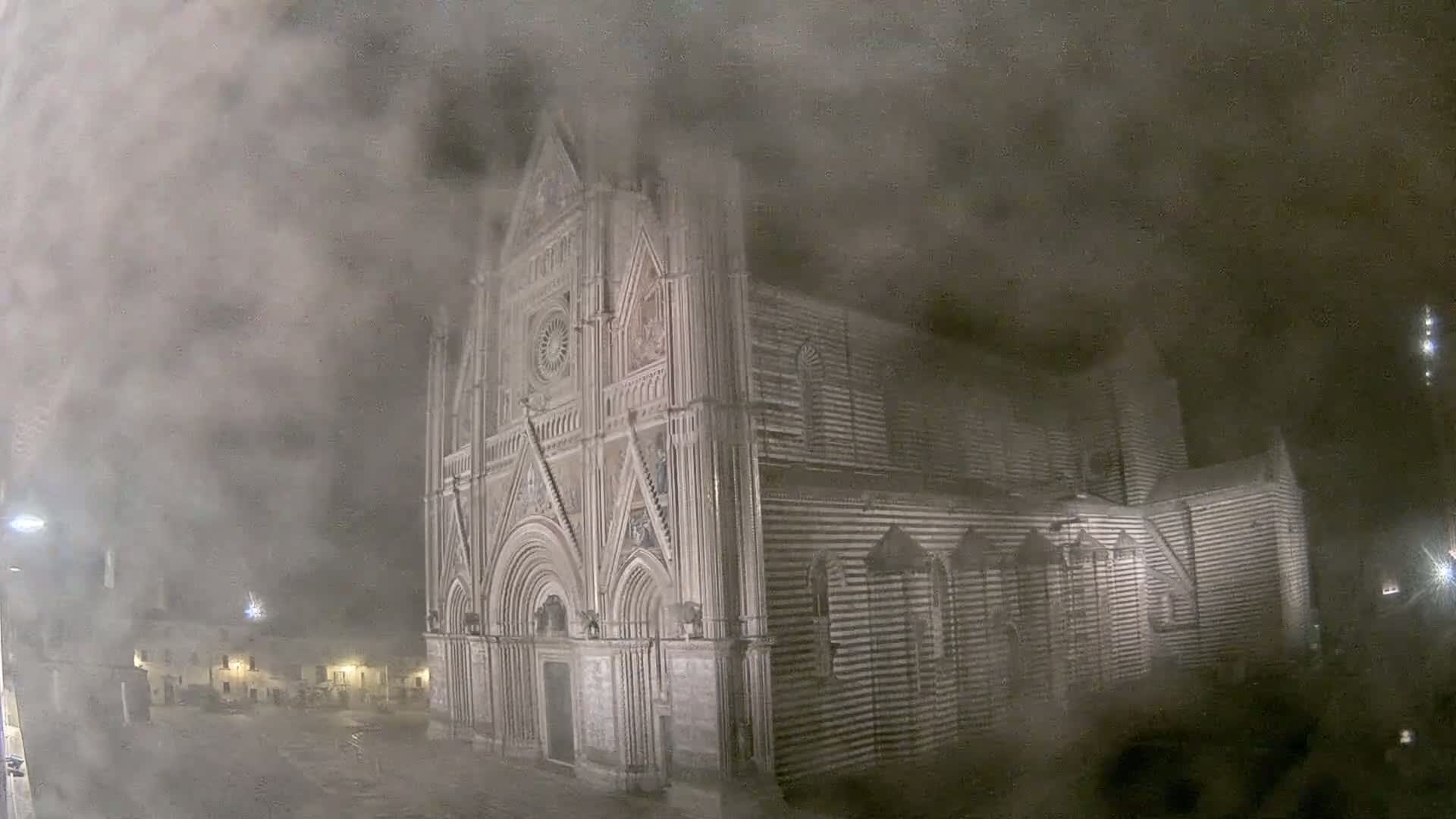 A large, striped stone cathedral is partially obscured by a thick fog at night.