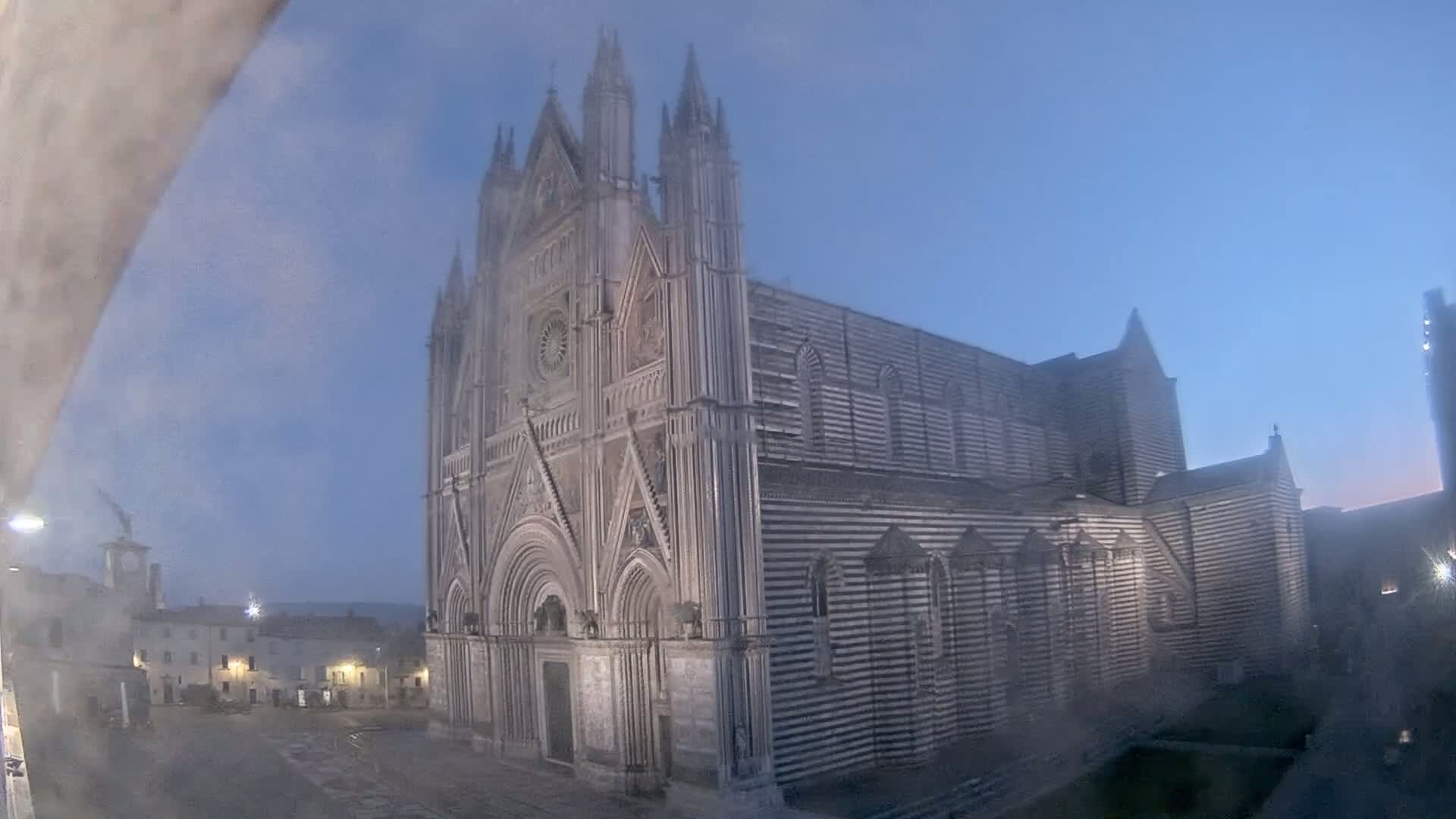 A large, striped cathedral stands in a town square under a hazy, dusky sky.