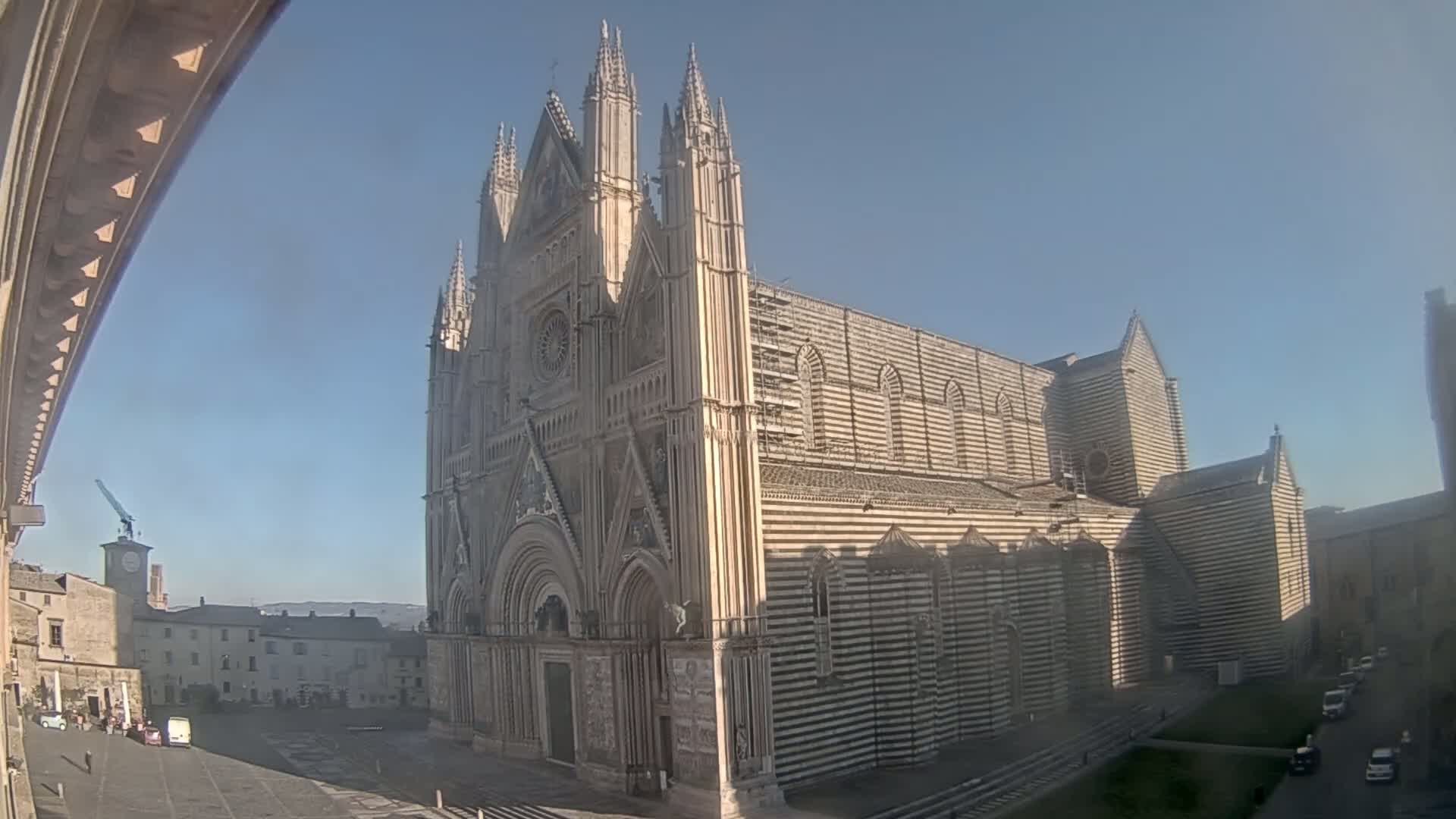 A large striped cathedral stands in a town square on a clear, sunny day.