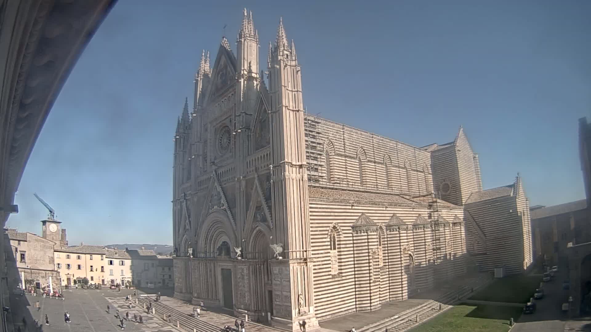 A large, striped cathedral stands in a town square on a sunny day.