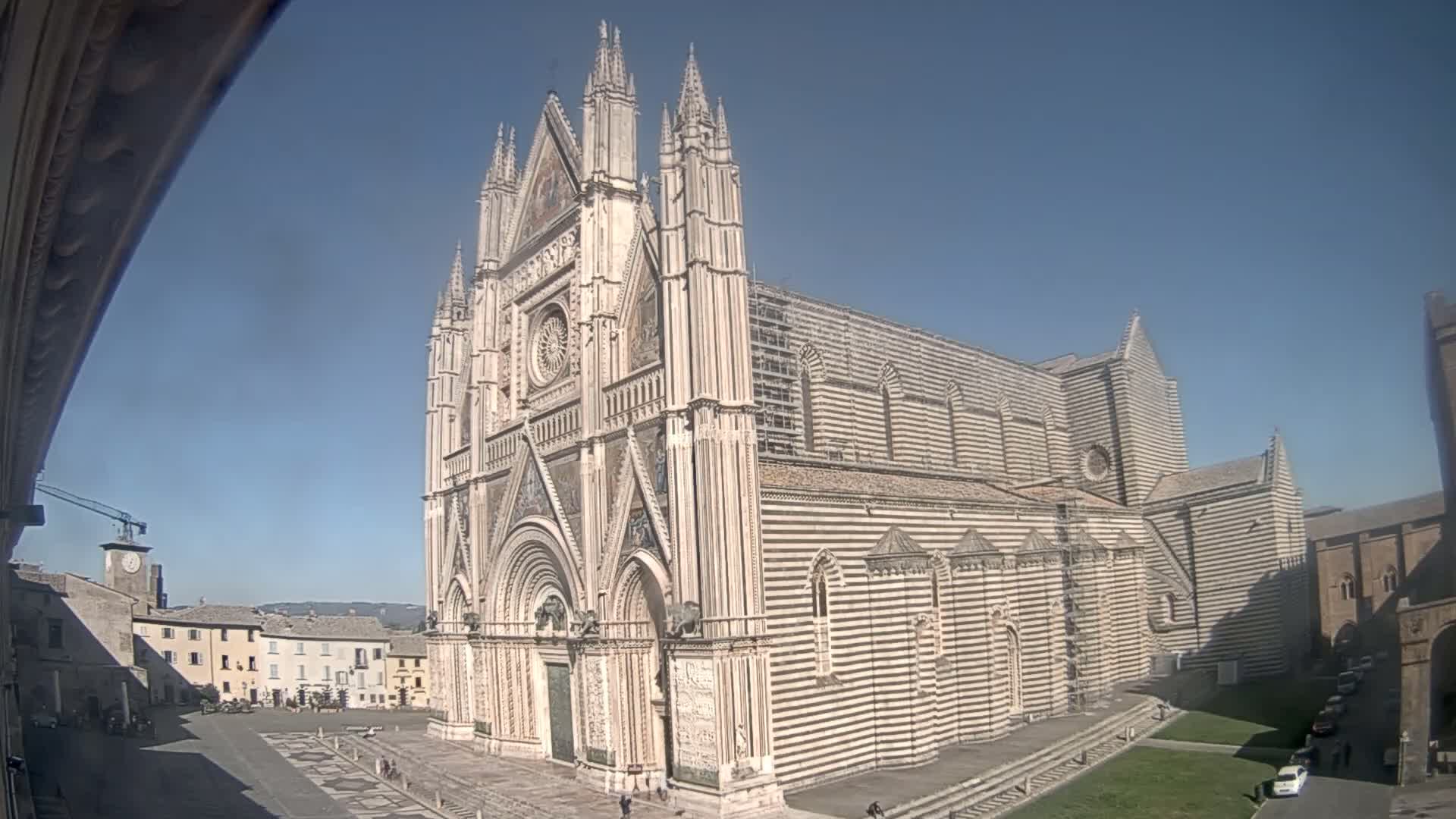 A large, striped cathedral stands in a town square on a sunny day.
