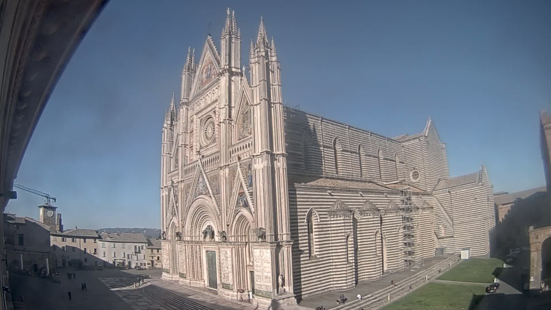 A large, ornate cathedral with black and white striped exterior walls stands in a plaza on a sunny day.