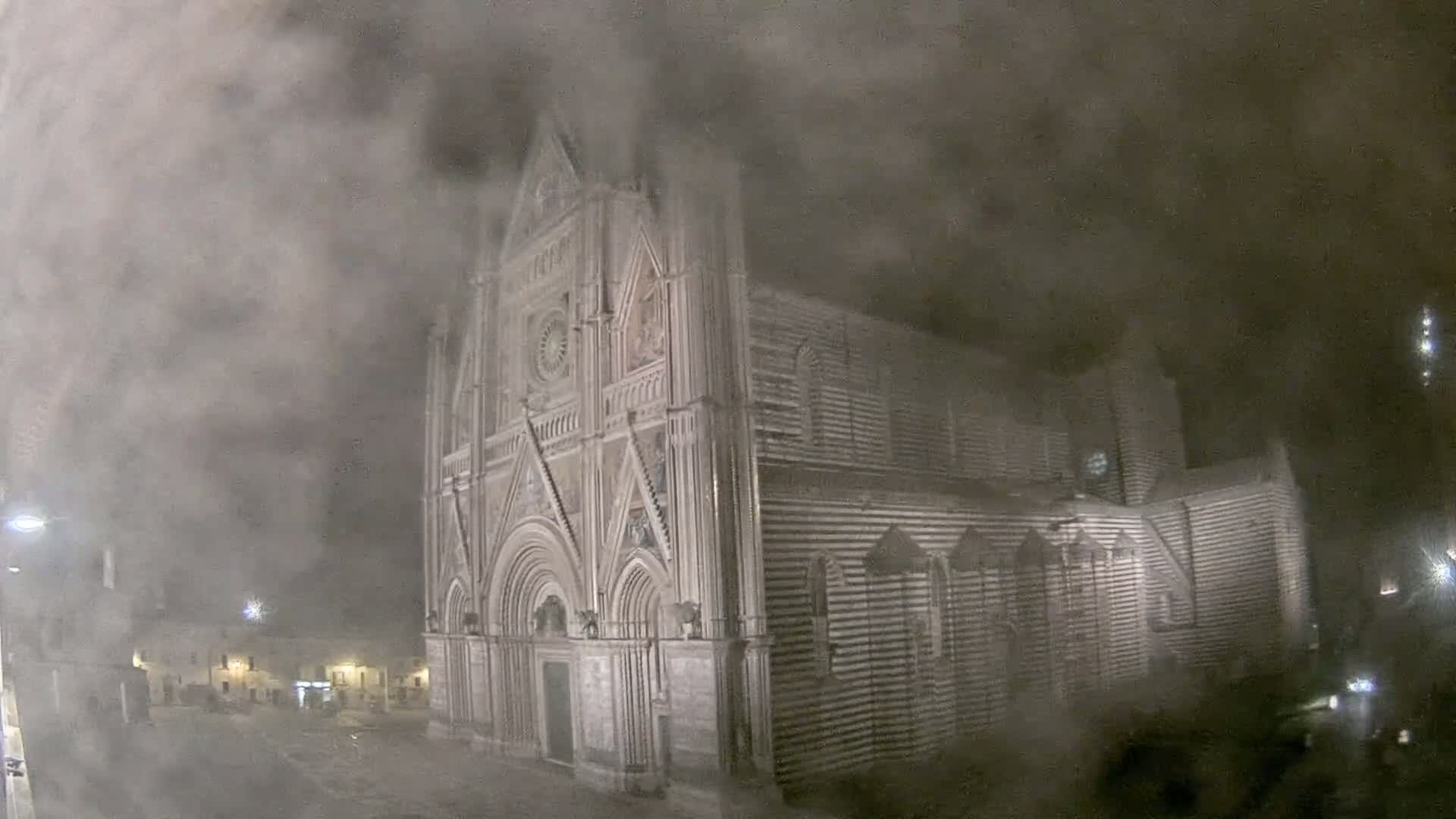 A large, ornate cathedral is partially obscured by a thick fog at night.